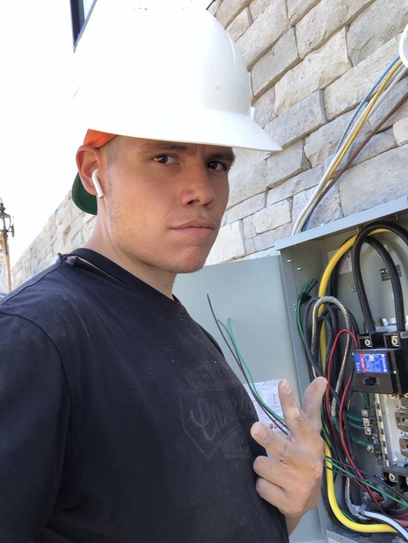 Mark Ortega in a hard hat, working at an open electrical panel.